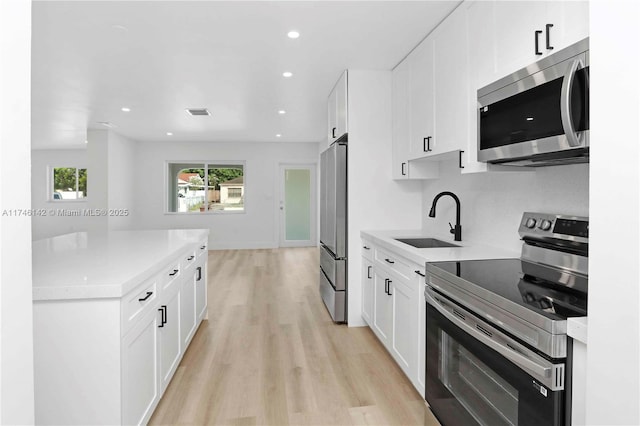 kitchen with white cabinetry, appliances with stainless steel finishes, sink, and light hardwood / wood-style flooring