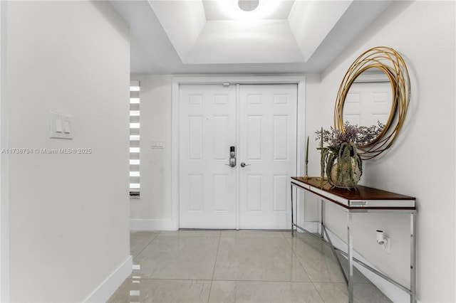 foyer featuring a raised ceiling, light tile patterned flooring, and baseboards