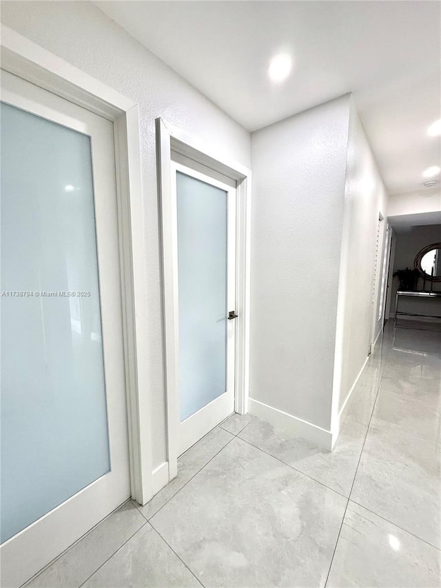 hall featuring light tile patterned floors, a textured wall, and baseboards