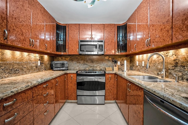 kitchen with light stone counters, a sink, appliances with stainless steel finishes, backsplash, and brown cabinets