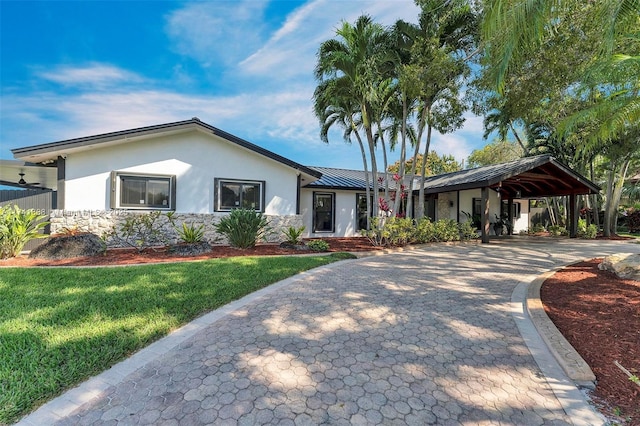 ranch-style house featuring a standing seam roof, a front lawn, decorative driveway, and stucco siding