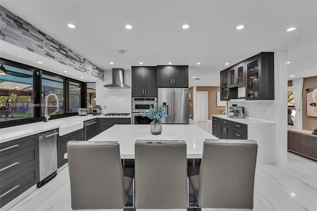 kitchen featuring stainless steel appliances, a sink, a center island, wall chimney exhaust hood, and glass insert cabinets