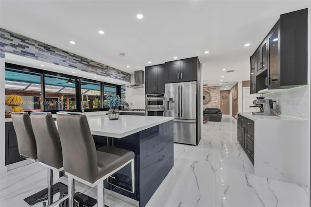 kitchen featuring recessed lighting, stainless steel appliances, marble finish floor, wall chimney range hood, and light countertops