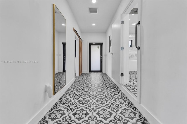 hallway with a barn door, visible vents, baseboards, and recessed lighting