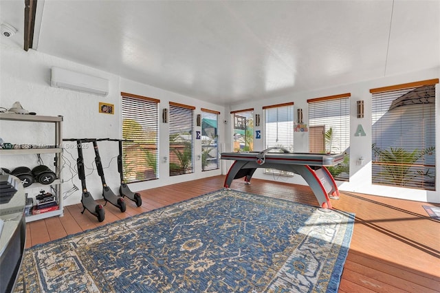 game room featuring a wall unit AC, wood-type flooring, and a wealth of natural light