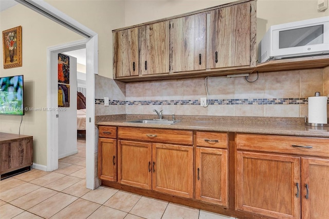 kitchen with tasteful backsplash, brown cabinetry, white microwave, a sink, and light tile patterned flooring