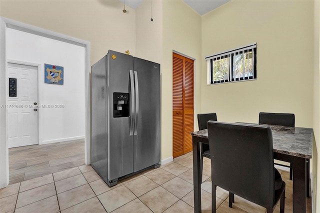 kitchen featuring baseboards, stainless steel refrigerator with ice dispenser, a high ceiling, and light tile patterned floors