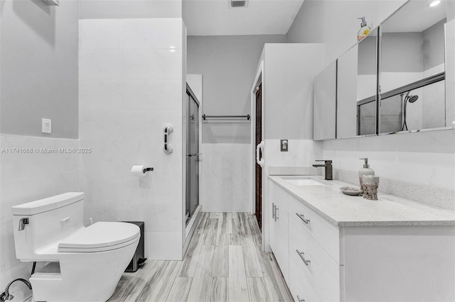 full bath with toilet, visible vents, vanity, tile walls, and a stall shower