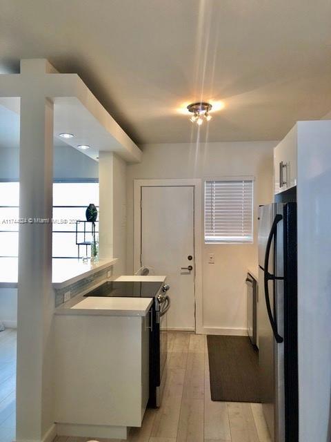 kitchen with stainless steel fridge, black range with electric stovetop, light hardwood / wood-style floors, white cabinets, and kitchen peninsula