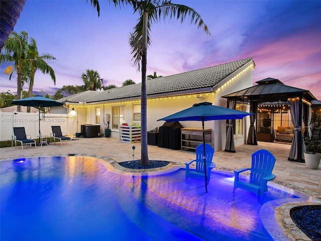 pool at dusk featuring a gazebo, cooling unit, and a patio area