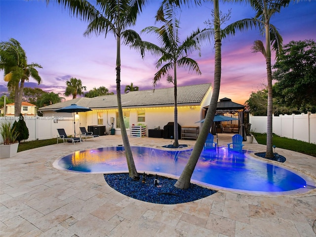 pool at dusk with a gazebo, a patio area, and pool water feature