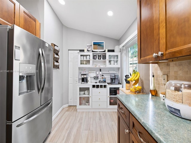 kitchen featuring backsplash, vaulted ceiling, and stainless steel refrigerator with ice dispenser