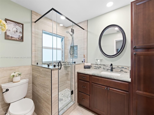 bathroom with vanity, toilet, a shower with shower door, and tile walls