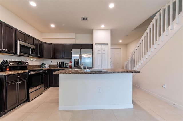 kitchen featuring a kitchen island with sink, light tile patterned floors, and stainless steel appliances