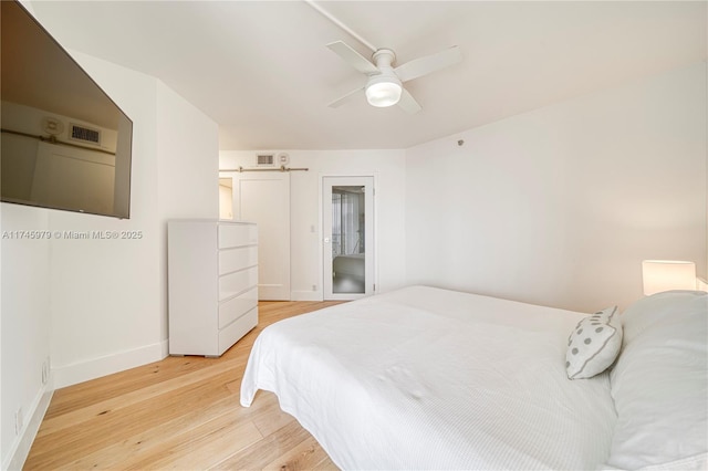 bedroom featuring a barn door, ceiling fan, and light hardwood / wood-style flooring