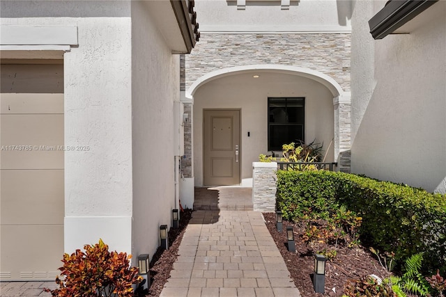 view of exterior entry featuring stone siding and stucco siding