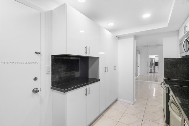 kitchen with white cabinets, stainless steel appliances, dark countertops, and light tile patterned floors