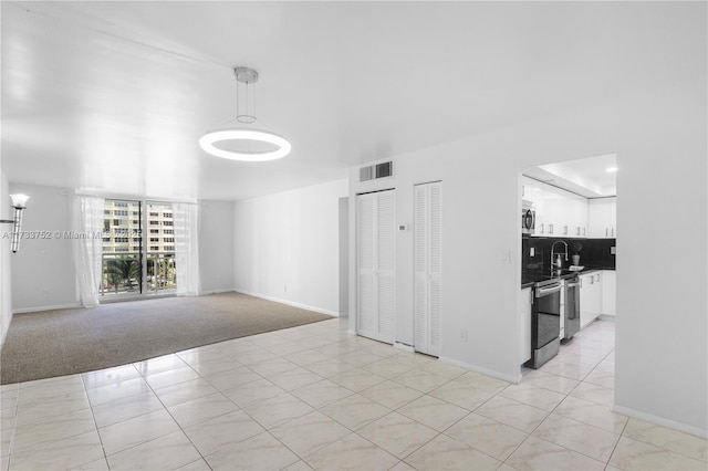 unfurnished room with light colored carpet, baseboards, light tile patterned flooring, a sink, and visible vents