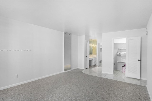 unfurnished bedroom with light carpet, baseboards, a walk in closet, and light tile patterned floors