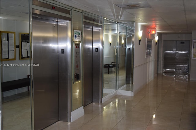 hallway featuring a drop ceiling, tile patterned flooring, and elevator