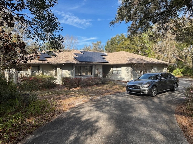 ranch-style home featuring roof mounted solar panels, driveway, and stucco siding