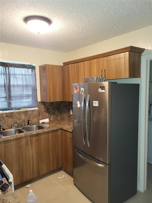 kitchen featuring sink, stone countertops, a textured ceiling, stainless steel fridge, and backsplash