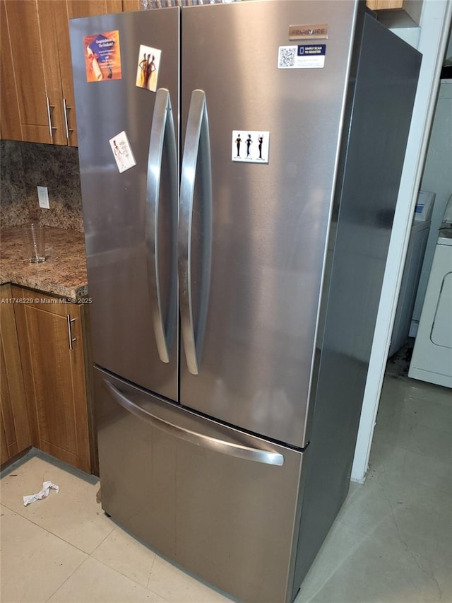 kitchen with washer / clothes dryer, dark stone countertops, backsplash, and stainless steel refrigerator