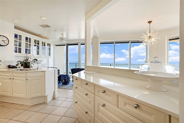 kitchen with light tile patterned floors, glass insert cabinets, light countertops, white cabinetry, and a sink