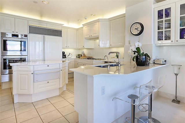 kitchen featuring paneled built in fridge, glass insert cabinets, double oven, a sink, and light tile patterned flooring