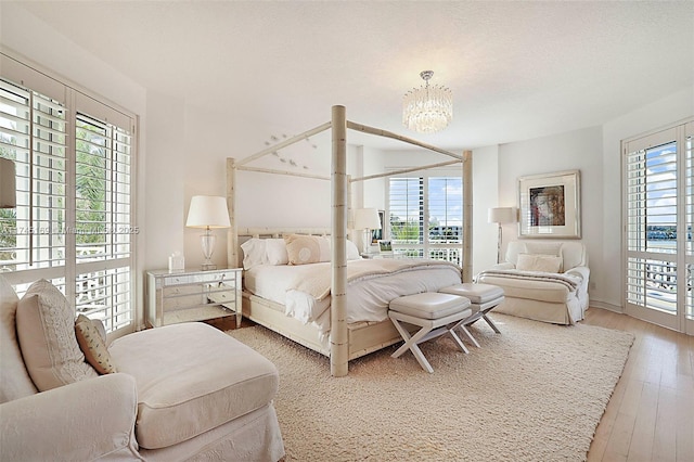 bedroom featuring access to outside, multiple windows, light wood finished floors, and an inviting chandelier