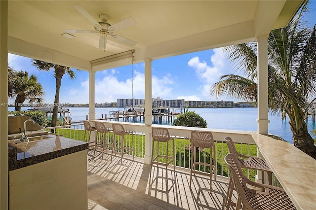 deck with outdoor wet bar, a water view, a sink, a ceiling fan, and exterior kitchen