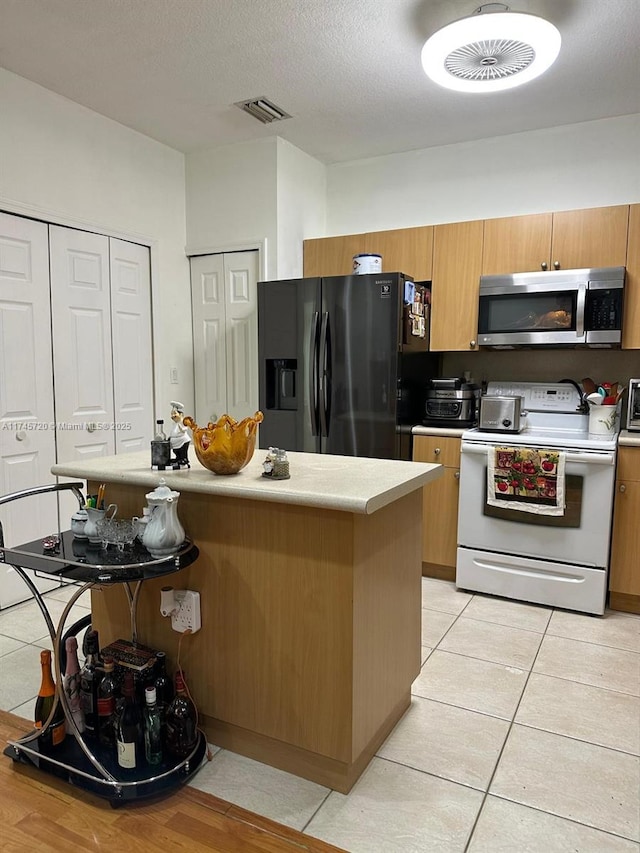 kitchen with light tile patterned floors, a center island, a textured ceiling, and appliances with stainless steel finishes