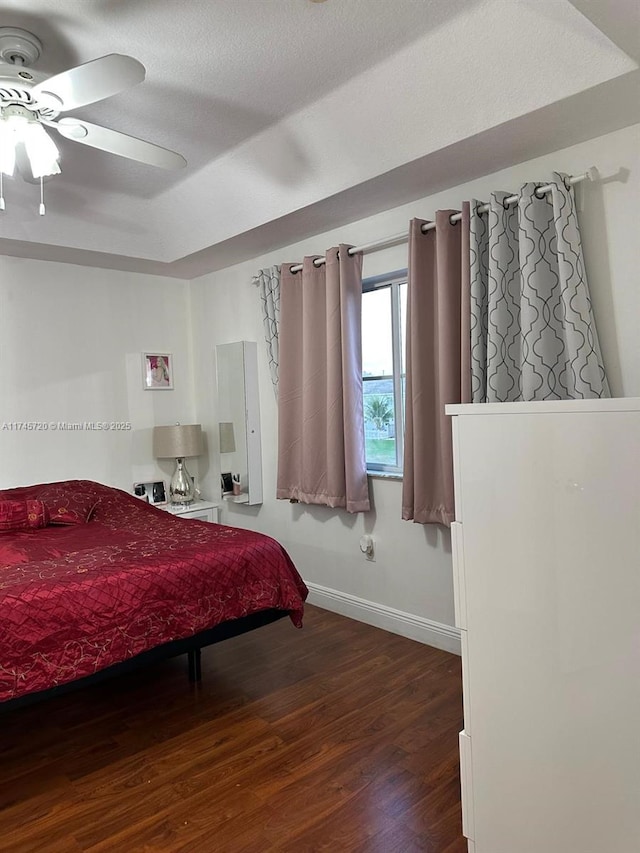 bedroom featuring ceiling fan, dark wood-type flooring, a textured ceiling, and a tray ceiling