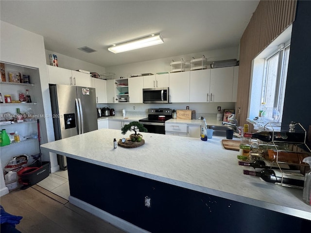 kitchen featuring stainless steel appliances, open shelves, light countertops, and white cabinetry