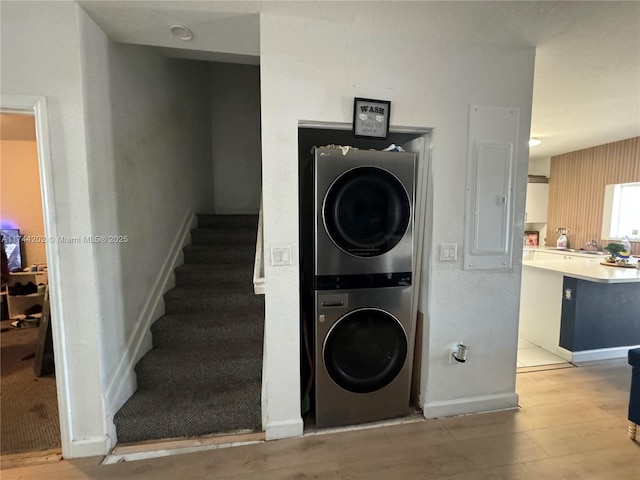 washroom featuring laundry area, baseboards, light wood-type flooring, electric panel, and stacked washer and clothes dryer