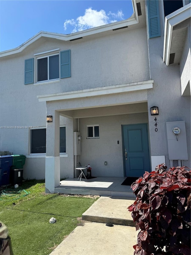 view of exterior entry with stucco siding, a lawn, and a patio