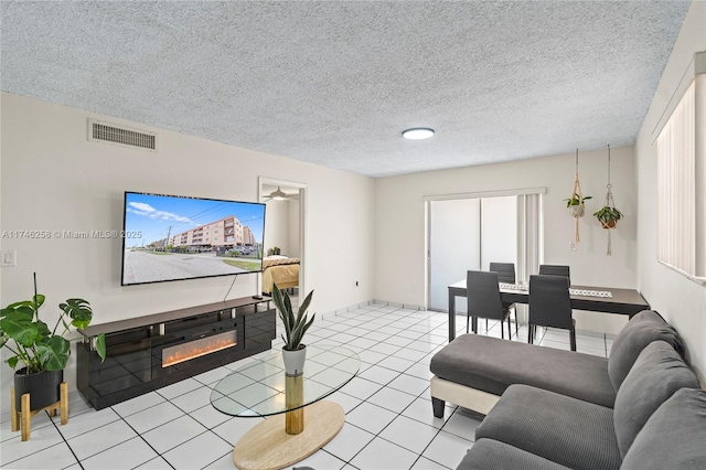 living area featuring a textured ceiling, light tile patterned flooring, a glass covered fireplace, and visible vents