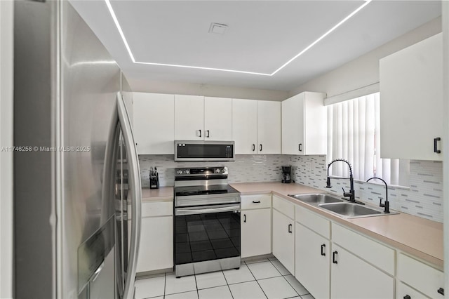 kitchen with light tile patterned flooring, sink, appliances with stainless steel finishes, decorative backsplash, and white cabinets