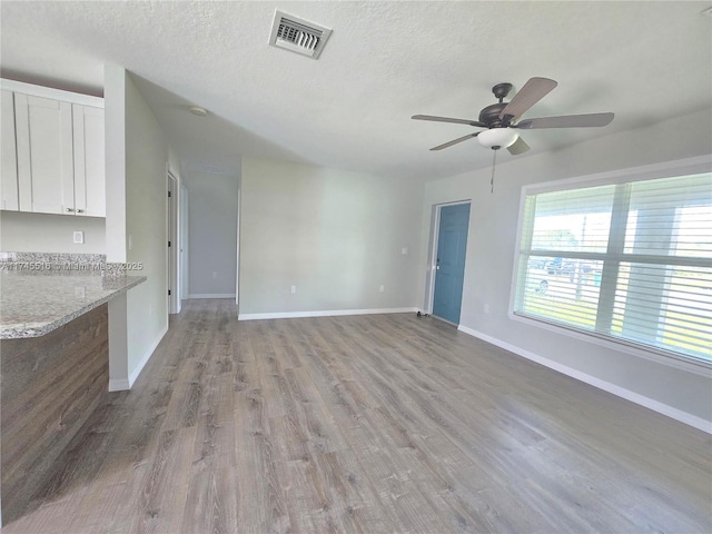 unfurnished living room with light wood finished floors, baseboards, visible vents, and a textured ceiling