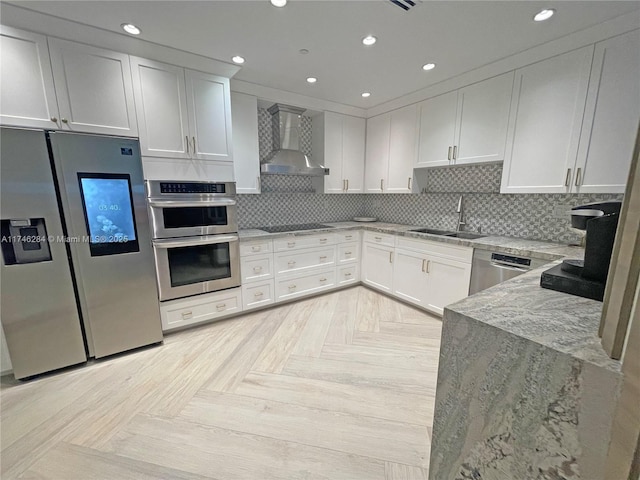 kitchen with wall chimney exhaust hood, sink, stainless steel appliances, light stone countertops, and white cabinets