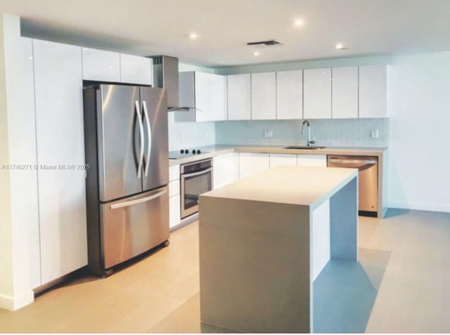 kitchen featuring appliances with stainless steel finishes, sink, white cabinets, a center island, and wall chimney exhaust hood