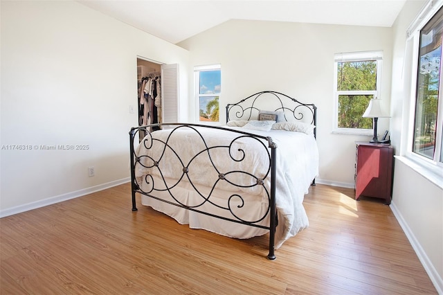 bedroom featuring a walk in closet, a closet, lofted ceiling, and light hardwood / wood-style flooring