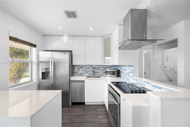 kitchen with white cabinetry, stainless steel appliances, stacked washer / dryer, ventilation hood, and kitchen peninsula