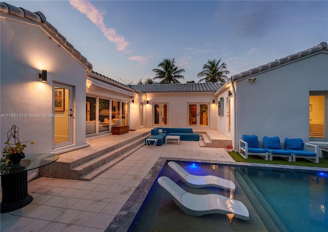 back of property at dusk featuring french doors, a patio area, a tile roof, and an outdoor living space