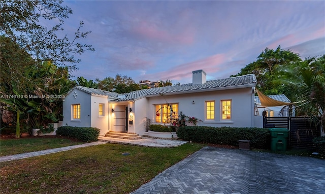 view of front facade featuring a tile roof, a chimney, a front lawn, and stucco siding