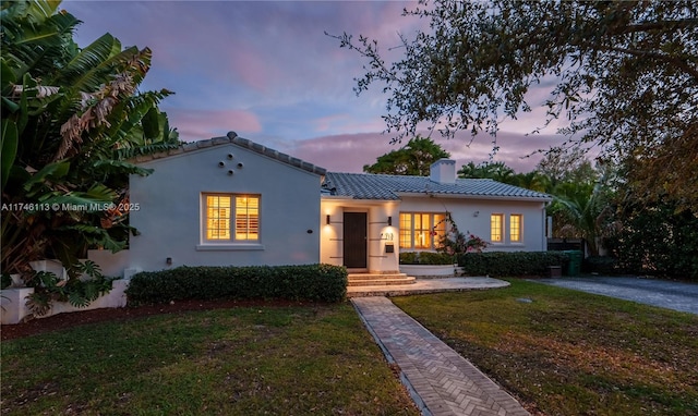 mediterranean / spanish-style house featuring stucco siding, a tile roof, a chimney, and a front yard