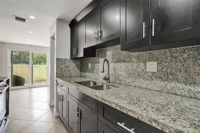 kitchen with sink, light tile patterned floors, stove, light stone countertops, and decorative backsplash