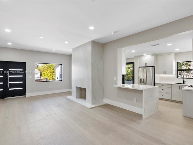 unfurnished living room with light wood-type flooring, recessed lighting, a sink, and baseboards