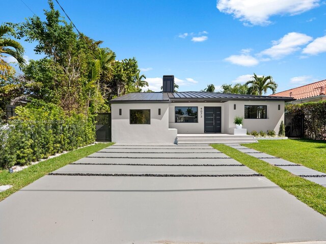 view of front of property with metal roof, stucco siding, a front lawn, a standing seam roof, and a chimney