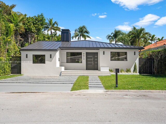 view of front of home featuring a chimney, metal roof, a standing seam roof, a front lawn, and stucco siding